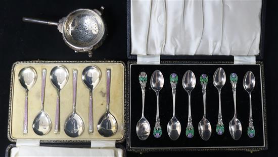 Two cased sets of silver and enamel spoons and a continental strainer.